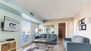 Sala de estar moderna com um sofá azul, uma mesa de centro de madeira e uma janela grande com vista para a cidade.