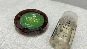 Una petita ampolla d'aigua mineral natural amb sabor a xocolata i un recipient rodó amb etiqueta verda.