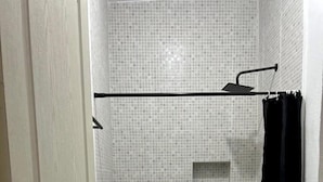 Un bany amb plat de dutxa emblenquinat, vàter blanc i cortina de bany negra.