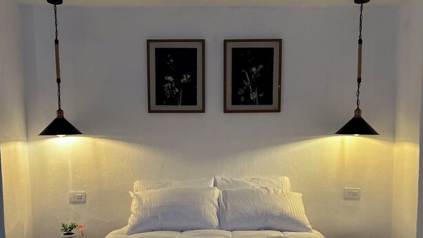 Un llit ben fet amb roba de llit blanca, dues taules de nit amb làmpades i dos quadres al mur.