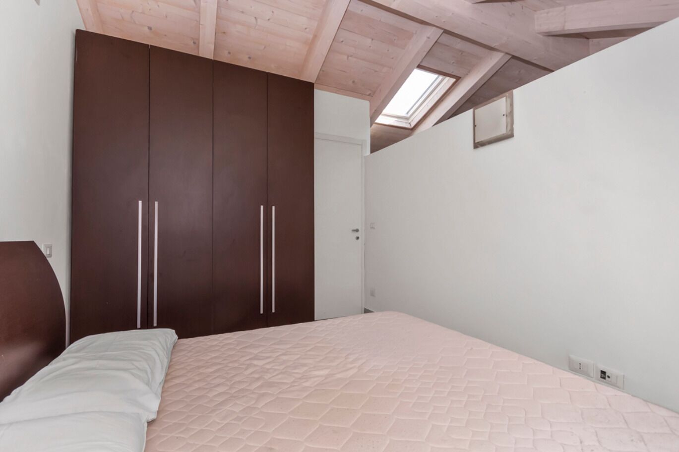 Een slaapkamer met een bed, een garderobe en een dakraam.