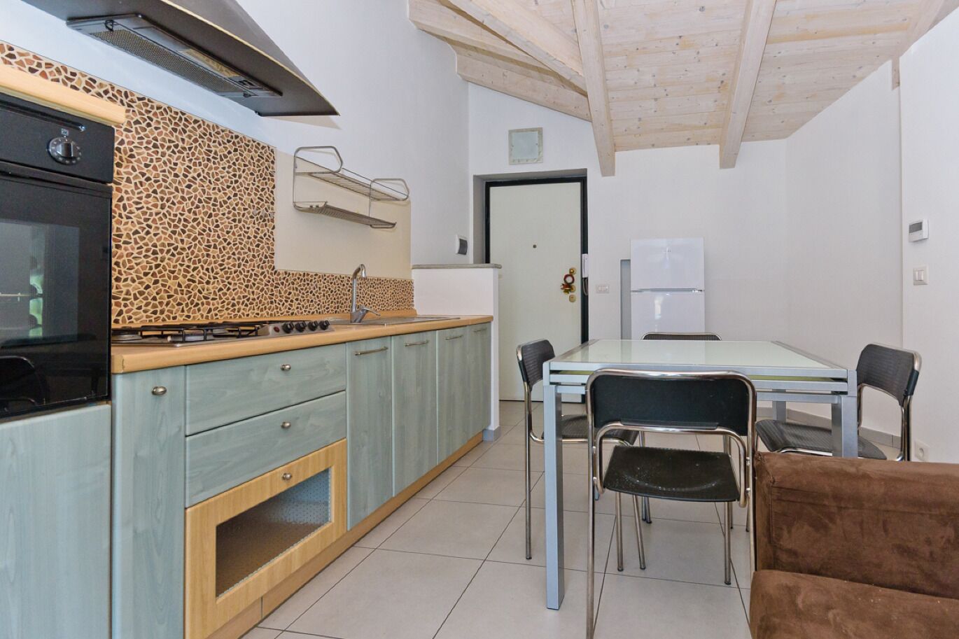 Une cuisine compacte équipée d’une cuisinière à gaz, d’un évier et d’un réfrigérateur. On y trouve également une table à manger avec quatre chaises.