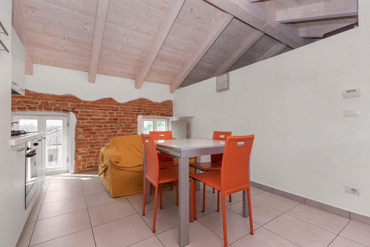 A dining area with a brick wall, a table with four orange chairs, and a yellow sofa.