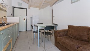 A compact kitchen with a dining table and chairs, a brown sofa, and a white refrigerator. - Casa a Pollenzo (Pollenzo)