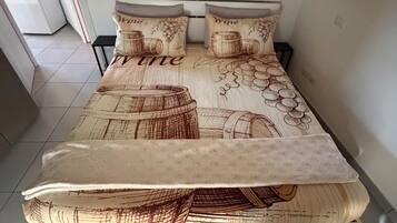 Una cama con una colcha de motivos relacionados al vino, una mesita de noche y una silla.