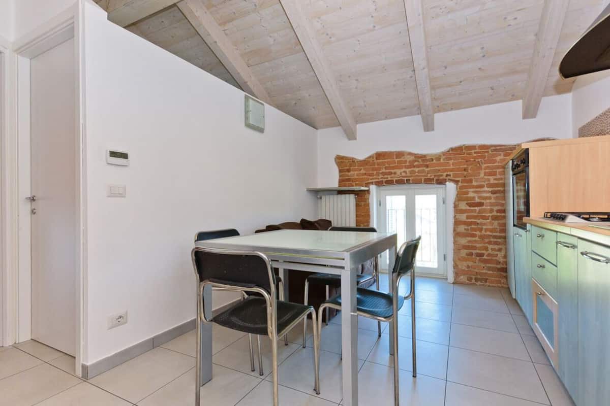 A dining area with a table and chairs, a kitchen with a brick wall, and a door leading to another room.