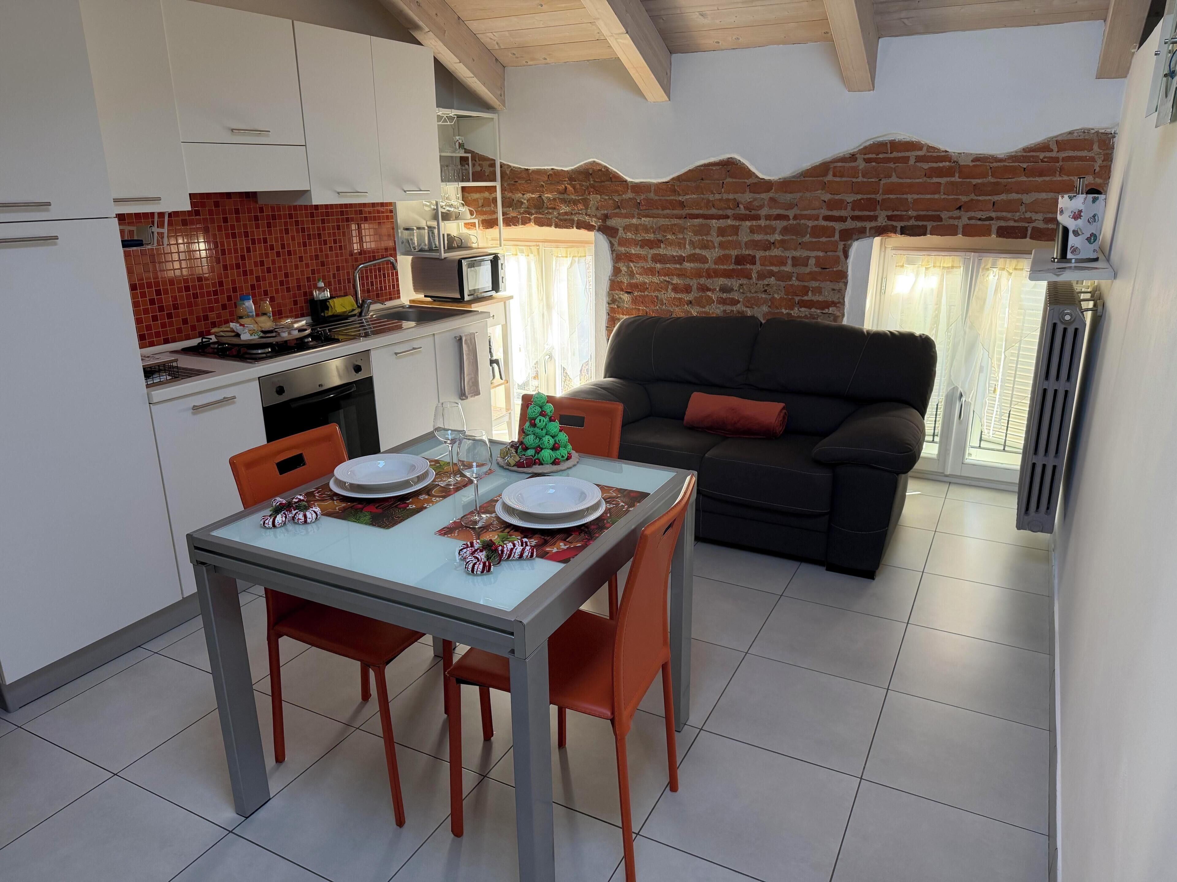 A dining area with a table set for four, a black sofa, and a brick wall.