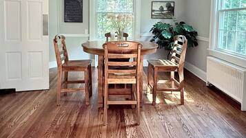 A dining area with a wooden table and chairs, a chandelier, and large windows with a view of greenery.