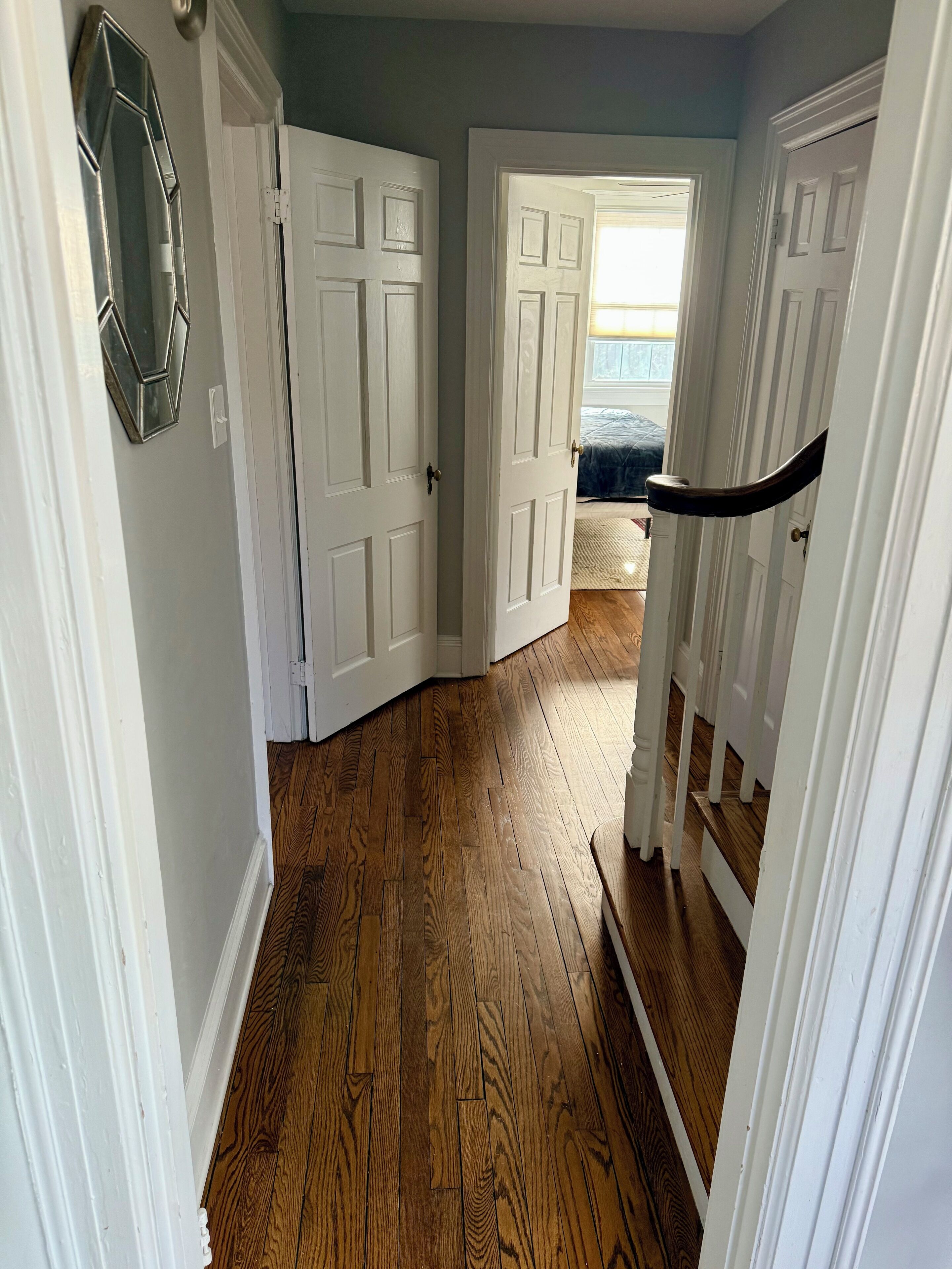 A hallway with wooden flooring, white doors, and a staircase leading to another room.