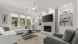 Una sala moderna con chimenea, sofás blancos y un televisor de pantalla plana.