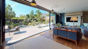 Un salon moderne doté d’une grande porte vitrée donnant sur un jardin, d’un canapé bleu, d’un meuble en bois et d’un lampadaire.