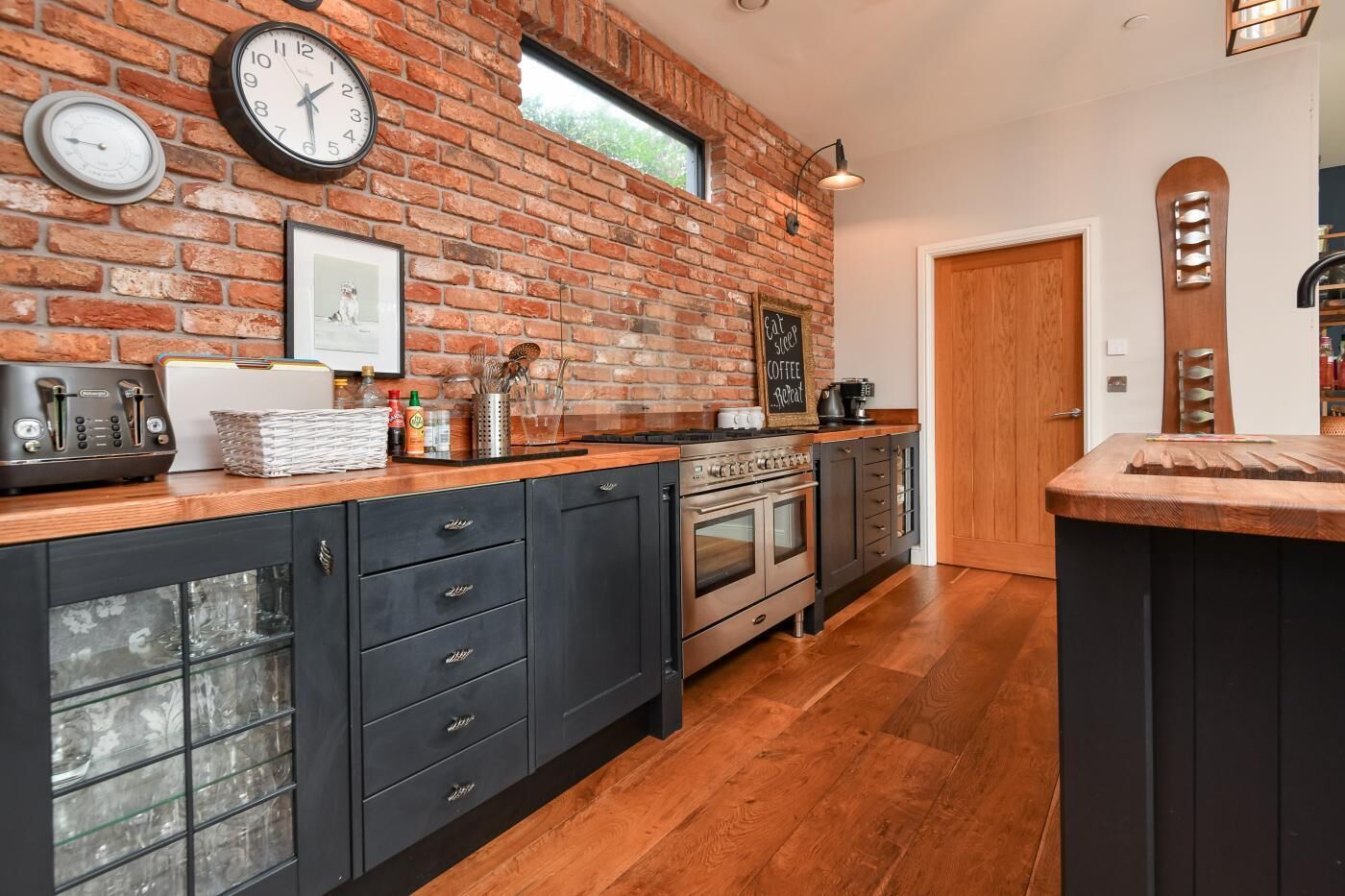 A kitchen with a brick wall, wooden cabinets, a stove, and a coffee machine.