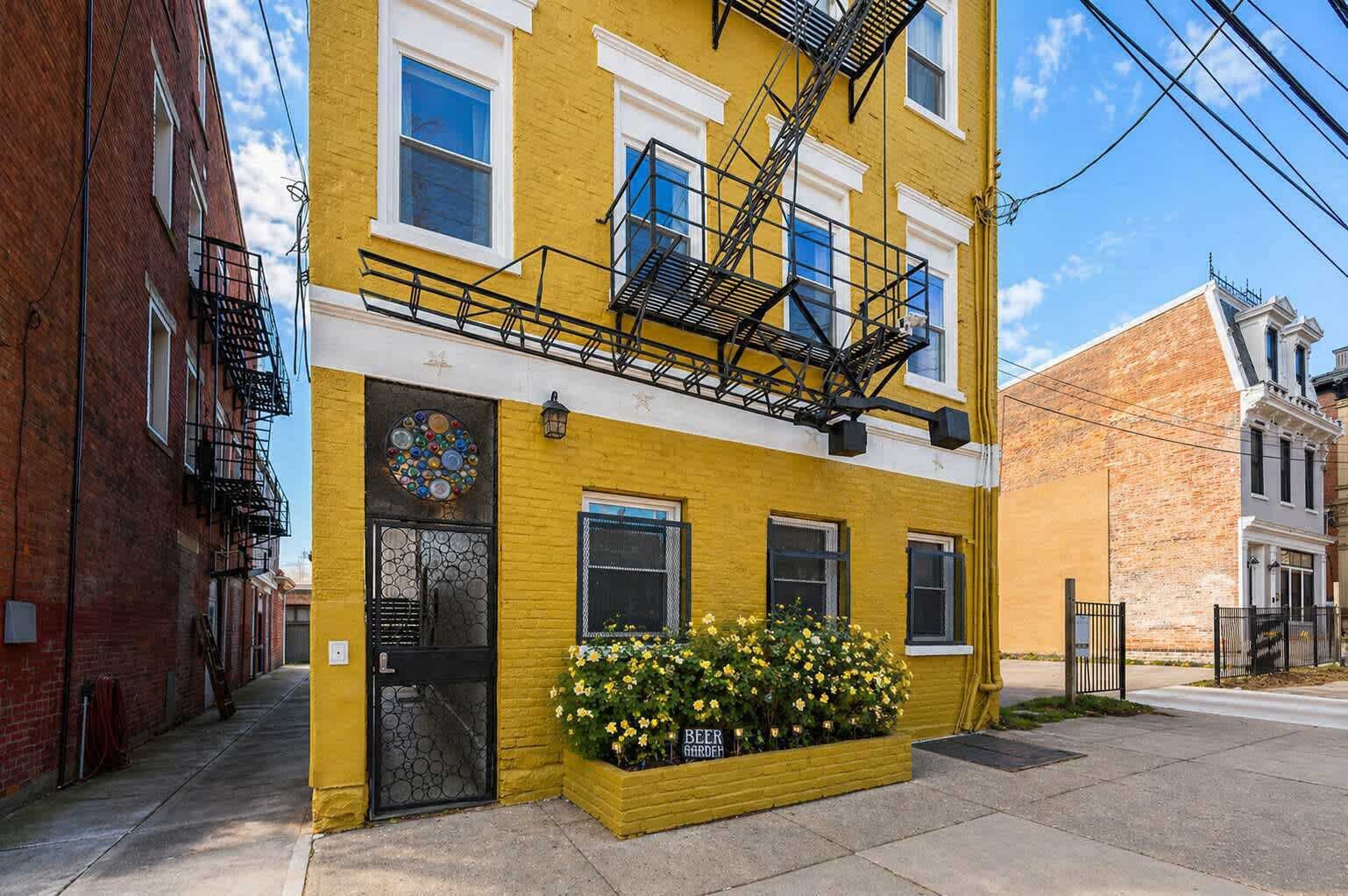 Un edificio amarillo con una escalera de incendios, una puerta con un diseño circular de vidrio y una jardinera con la leyenda 'Beer Garden'.