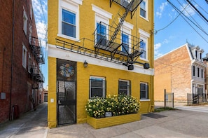 A yellow building with a fire escape, a door with a circular glass design, and a flower box labeled 'Beer Garden'. - Bright OTR Loft - Walk to Rhinegeist and Free Parking (Cincinnati)