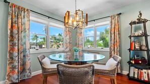 A dining area with a round glass table, wicker chairs, a chandelier, and a bookshelf with books and decorative items. - Sunny Tropical 3BR/3BA Retreat With Private Pool in Bonita Springs (Bonita Springs)