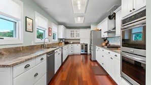 A modern kitchen with white cabinets, granite countertops, and a wooden floor. - Sunny Tropical 3BR/3BA Retreat With Private Pool in Bonita Springs (Bonita Springs)