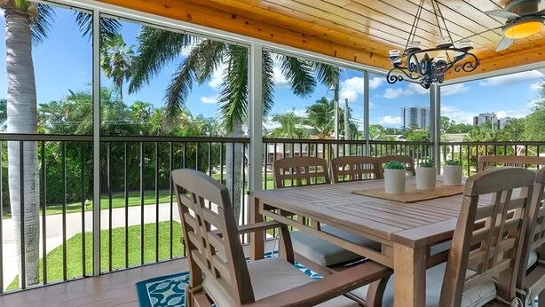 A wooden deck with a table and chairs, a hanging light fixture, and a view of palm trees and buildings. - Sunny Tropical 3BR/3BA Retreat With Private Pool in Bonita Springs (Bonita Springs)