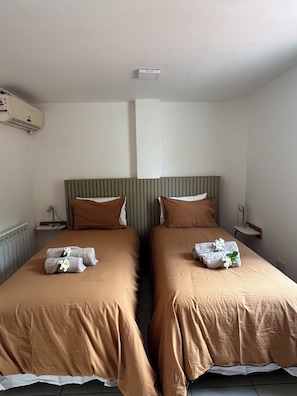 A hotel room with two beds, each with a brown bedspread and pillows, a headboard, bedside tables, and a wall-mounted air conditioning unit. - Family Chalet Boutique (Luján de Cuis)