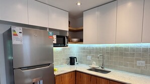 A modern kitchen with a stainless steel refrigerator, a microwave, wooden cabinets, a sink, and a tiled backsplash.