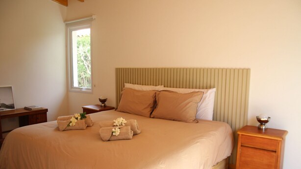 A bedroom with a large bed, a bedside table with a lamp, a window, and a small desk with a chair.
