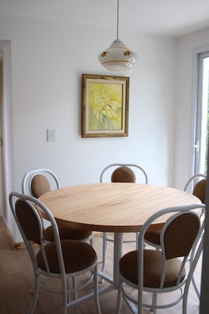 A dining area with a round wooden table, six metal chairs, and a hanging pendant light.