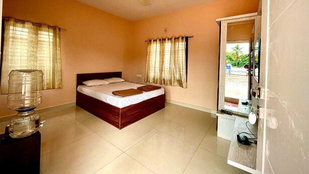 A bedroom with a bed, curtains, a water dispenser, a mirror, and a view of the outside. - Bricknest Homes (Mysore)
