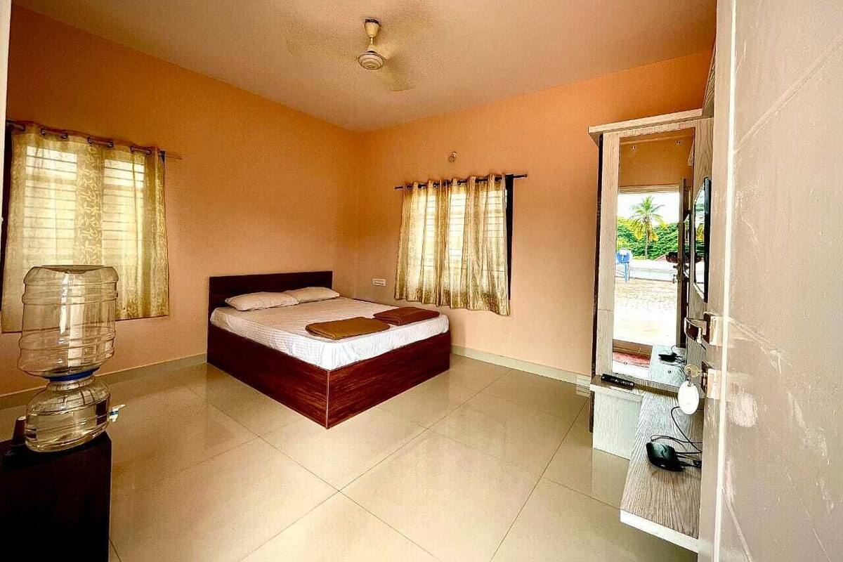 A bedroom with a bed, curtains, a water dispenser, a mirror, and a view of the outside.