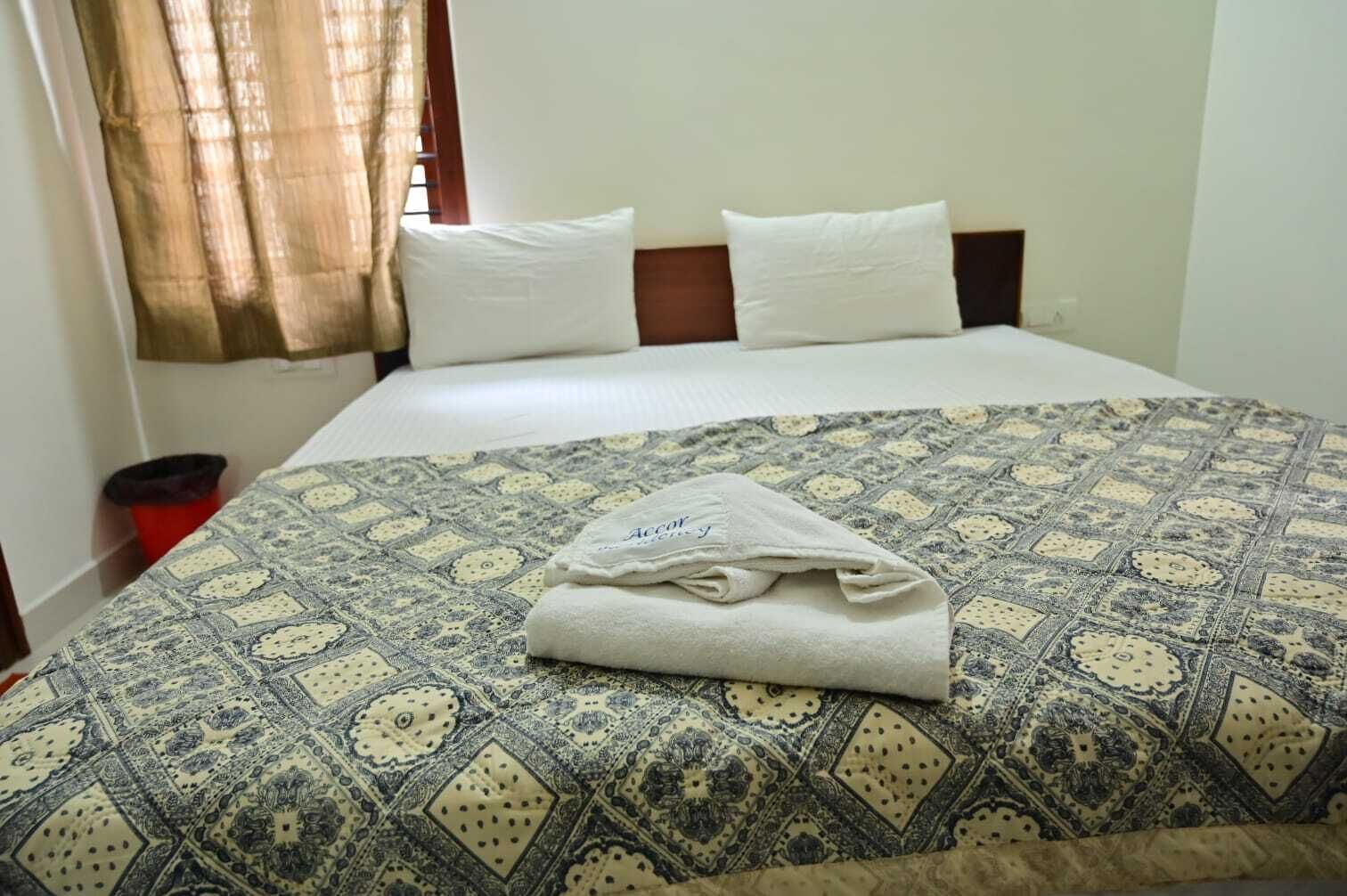 Una cama bien hecha con una colcha estampada, dos almohadas y una toalla doblada sobre la cama.