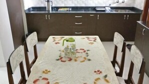 A dining area with a table set for four, surrounded by wooden chairs. - Bricknest Homes (Mysore)