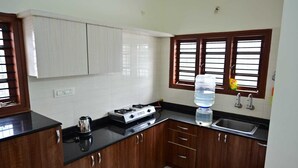 A kitchen with wooden cabinets, a gas stove, a sink, and a window with blinds. - Bricknest Homes (Mysore)