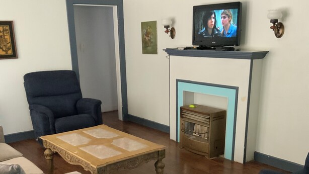 Olohuoneessa on televisio, takka, sininen nojatuoli, puinen sohvapöytä ja harmaa sohva.