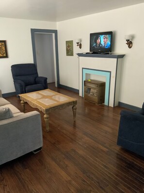 A living room with a television, a fireplace, a blue armchair, a wooden coffee table, and a grey sofa. - Cozy Three Bedroom House In Scenic Rusk. (Rusk)