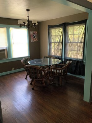 A dining area with a round glass table surrounded by wicker chairs, a chandelier, and large windows with sheer curtains. - Cozy Three Bedroom House In Scenic Rusk. (Rusk)