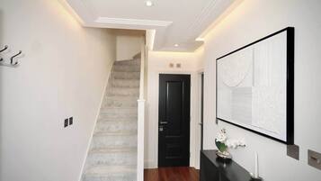 A hallway with a staircase, a black door, a wall-mounted artwork, and a small table with a candle and flowers.