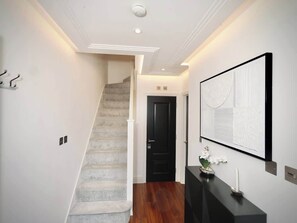 Un corridoio con una scala, una porta nera, un'opera d'arte appesa al muro e un tavolino con una candela e fiori.