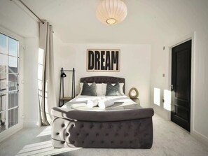 A bedroom with a large bed, a wall-mounted artwork labeled 'DREAM,' a window with curtains, and a door. - Large 4BR Home w/3 Baths I Sleeps 9 I Free Parking (South Croydon)