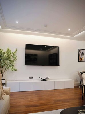 Un salon moderne avec un grand téléviseur à écran plat fixé au mur, un meuble de rangement blanc en dessous, un plancher en bois et une plante en pot.