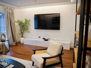 Een moderne woonkamer met een flatscreen televisie, een bank, een salontafel en een potplant.