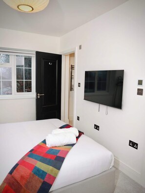 Een slaapkamer met een bed, een aan de muur bevestigde televisie, een deur en een raam.
