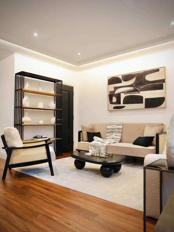 A modern living room with a sofa, a black and white abstract painting, a black bookshelf, and a wooden coffee table.