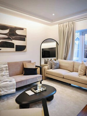 A modern living room with two sofas, a coffee table, a large abstract painting, a mirror, and a window with curtains. - Large 4BR Home w/3 Baths I Sleeps 9 I Free Parking (South Croydon)