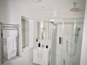 Un bagno moderno con cabina doccia in vetro, un lavandino bianco e un portasciugamani.