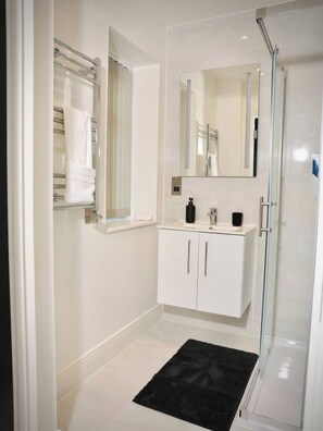 Une salle de bain moderne avec une douche à l’italienne en verre, des meubles blancs et un tapis noir.