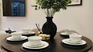 A round dining table with white bowls and black saucers, a black vase with green plants, and a framed picture on the wall.