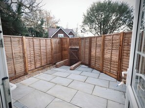 Een terras met een houten hek, een bakstenen oprit en een huis op de achtergrond.