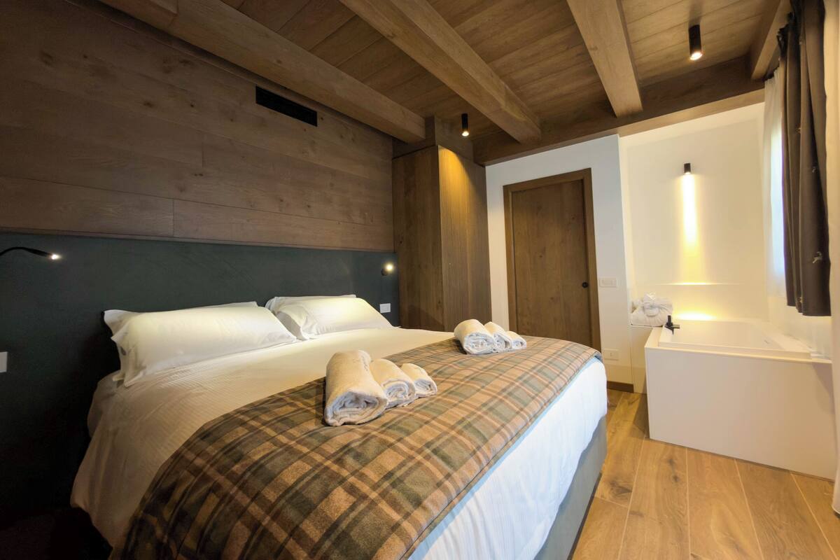 Una habitación de hotel con techo de madera, una cama con colcha escocesa, una mesita de noche con lámpara y una puerta.
