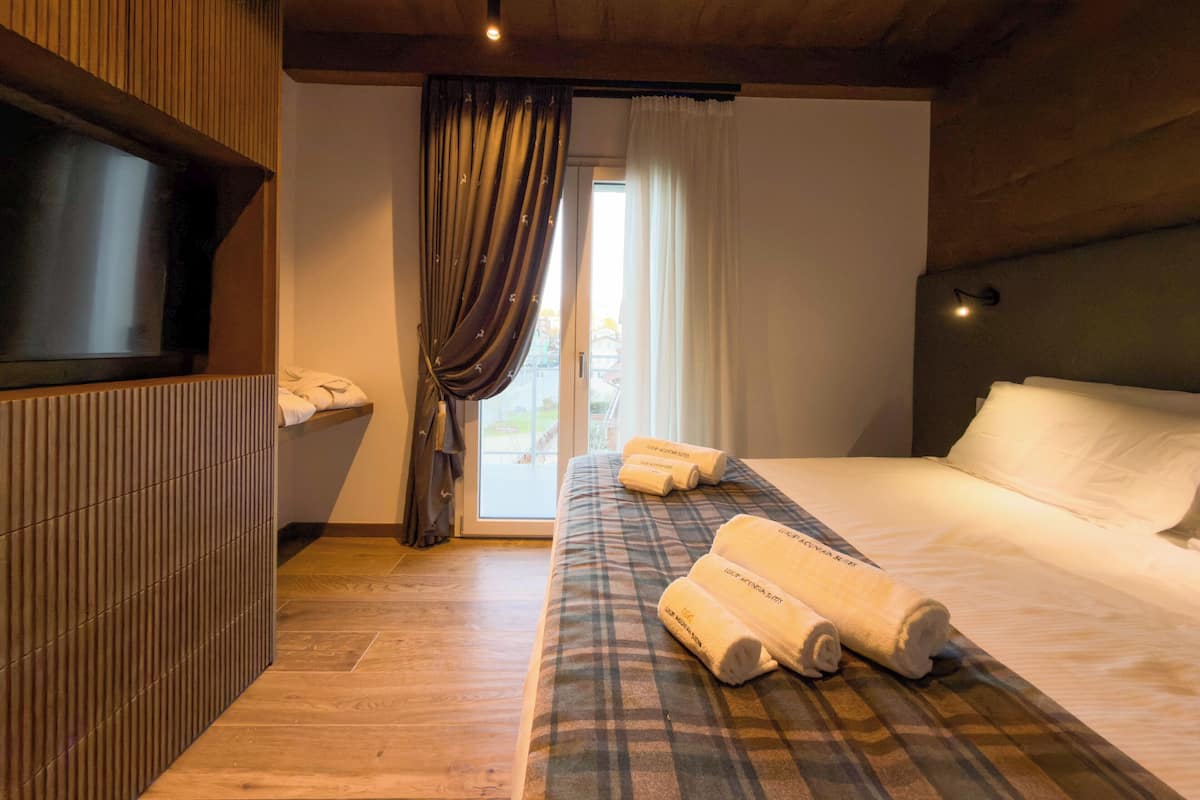 Habitación de hotel con cama, televisión, pared de paneles de madera, ventana con cortinas y vista al exterior.