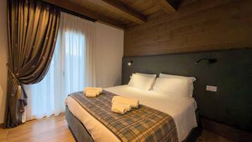 A hotel room with a wooden ceiling, a bed with white linens, a plaid blanket, and a window with curtains.