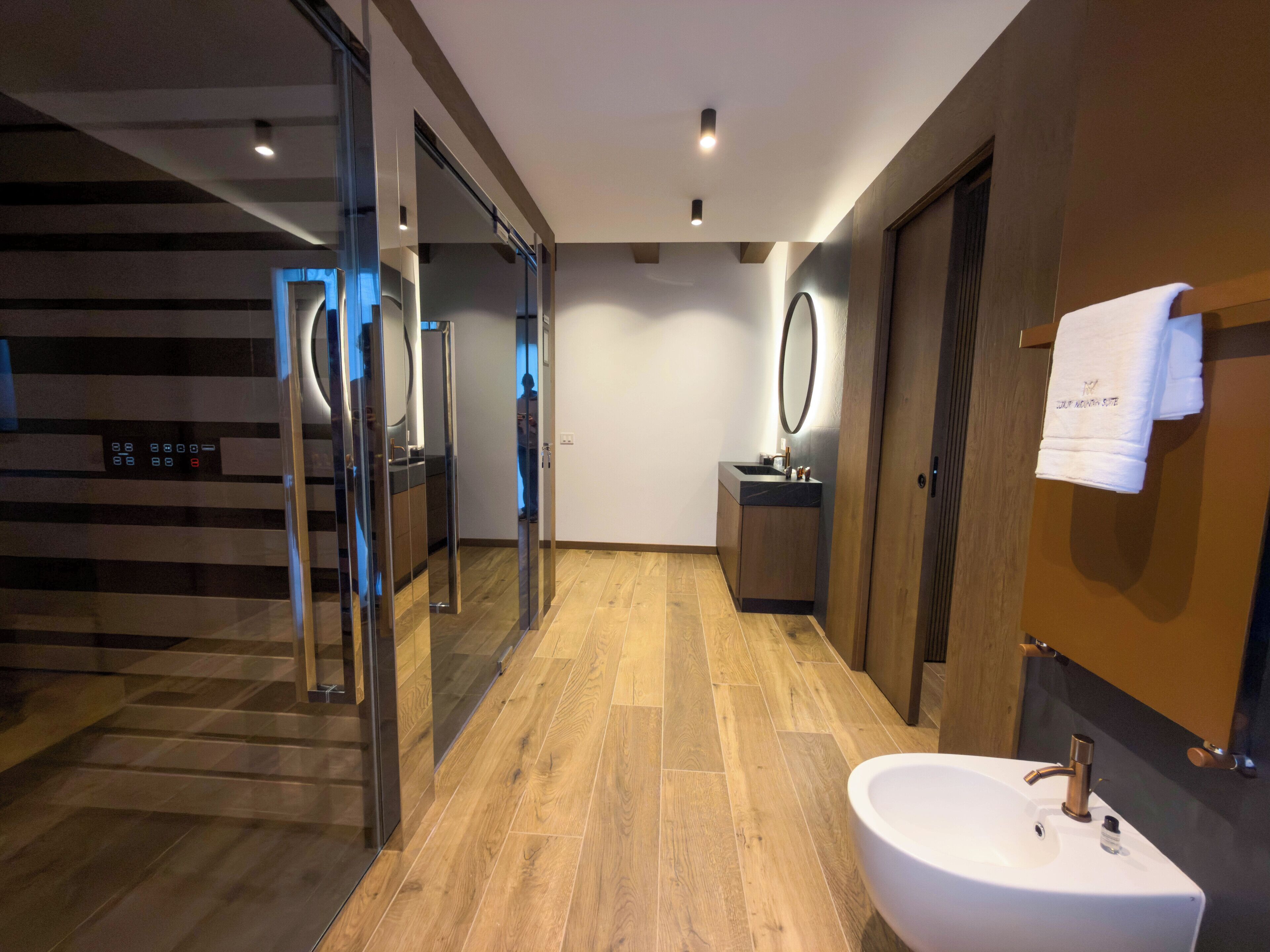 Ein modernes Badezimmer mit Holzboden, einem weißen Waschbecken und einem Spiegel.