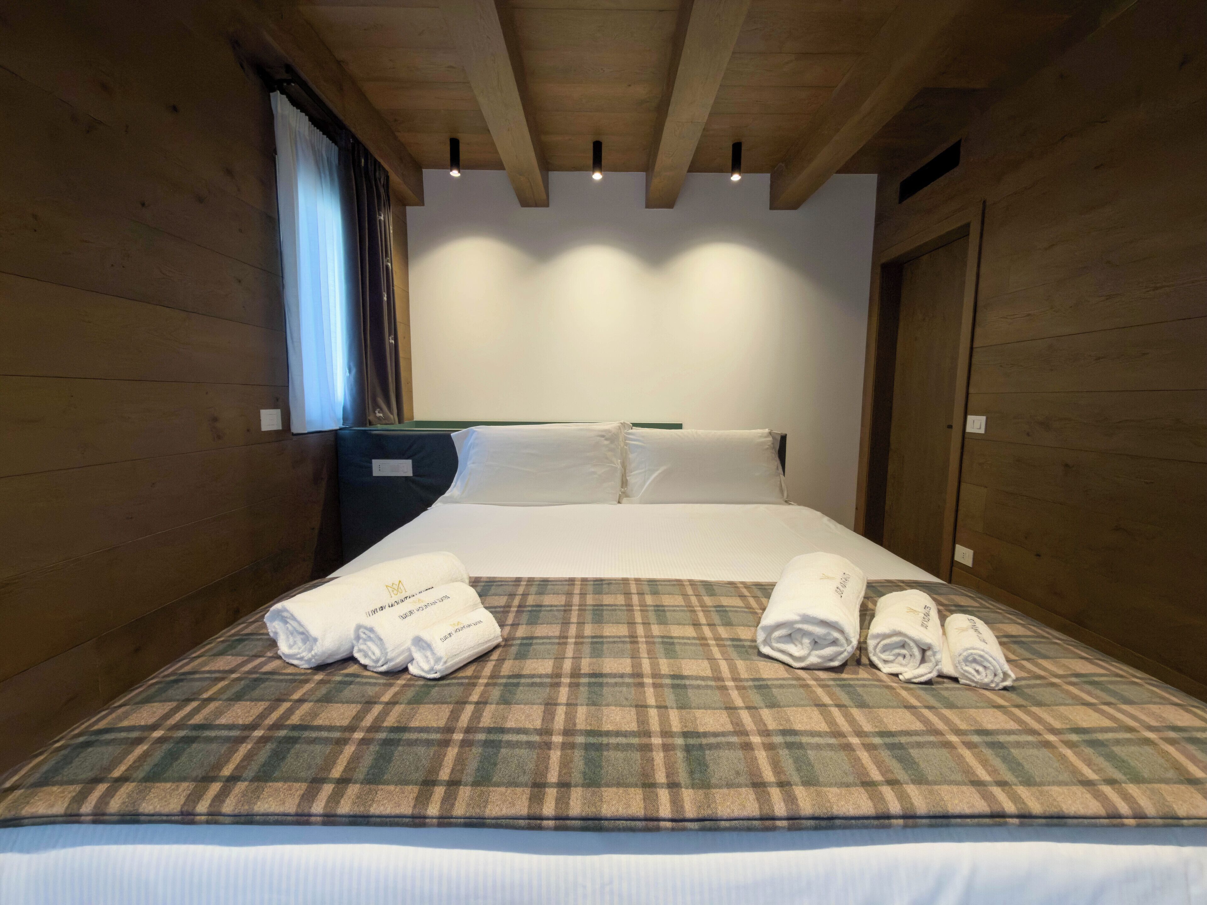 A hotel room with a plaid bedspread, neatly folded towels, and wooden walls.